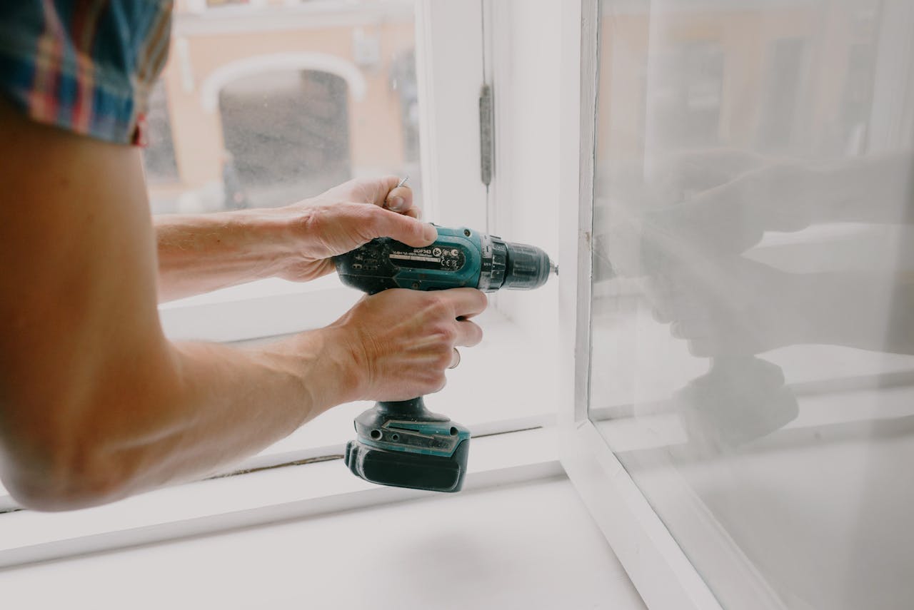 about-us A person using an electric drill to repair or install a window indoors.